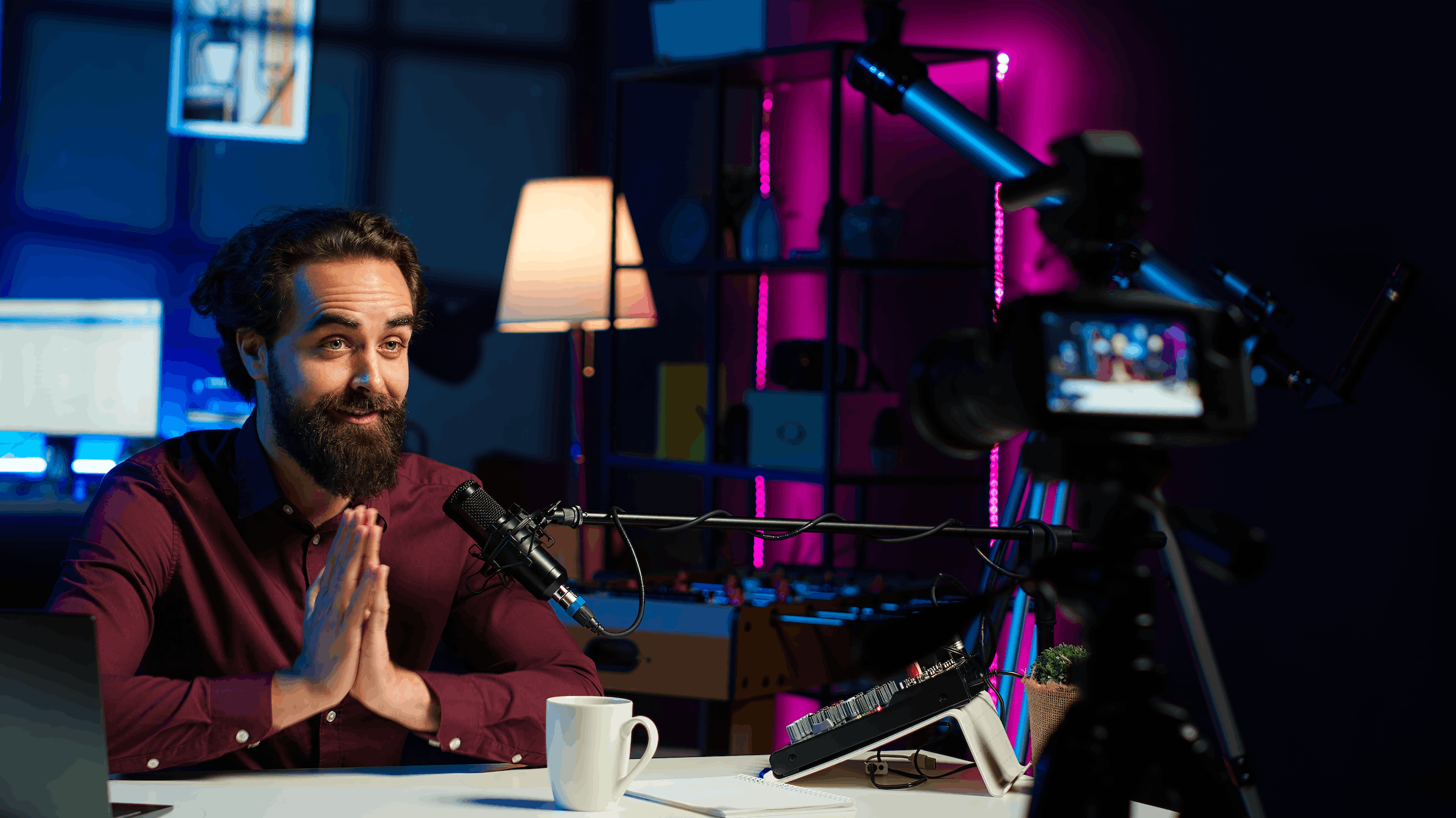 A bearded presenter speaking into a studio microphone in front of a video camera in a softly lit content studio