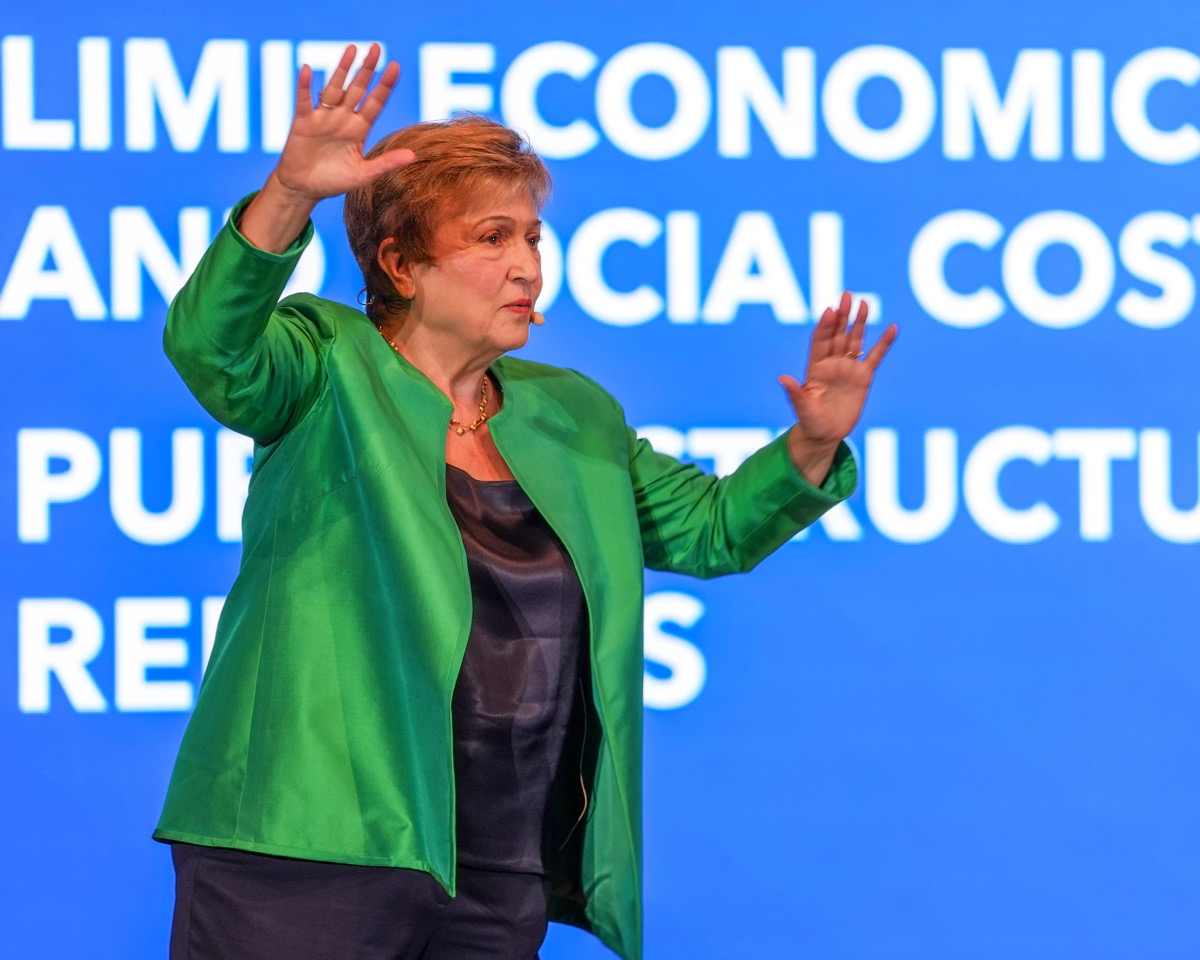 A delegate speaking at a podium during an international finance conference, with microphones and a conference backdrop visible