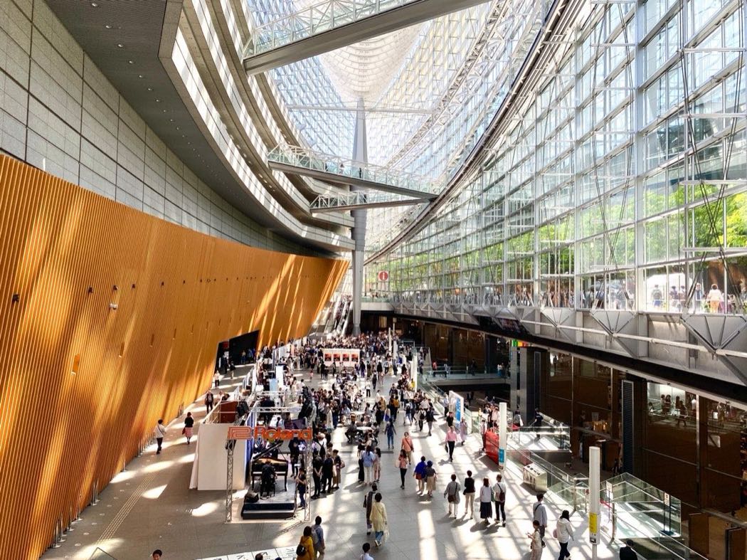 The vast glass and steel interior of a modern conference and event hall in Asia, filled with people during a business gathering
