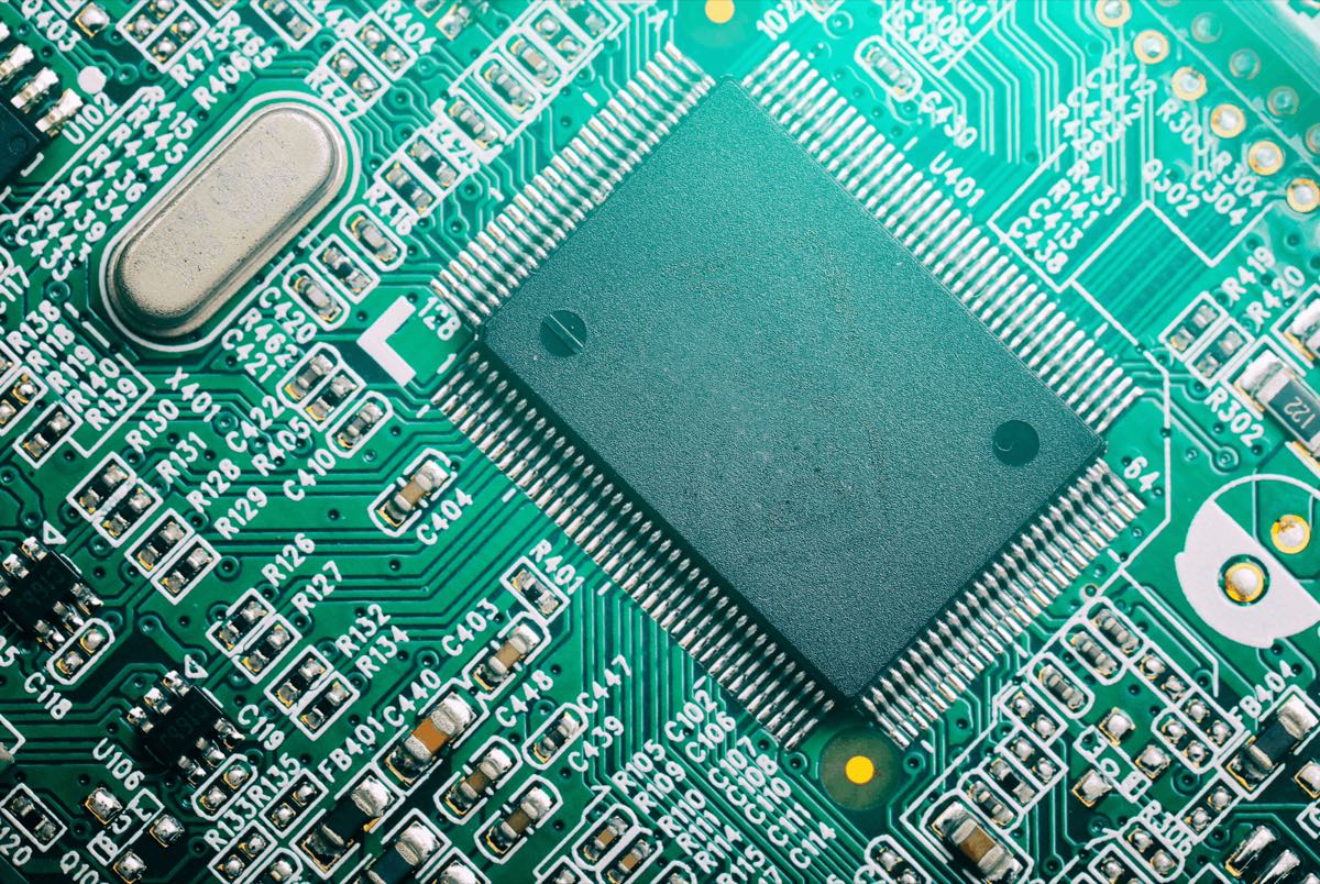 Close up of a green printed circuit board with a large microchip surrounded by densely labelled components and traces
