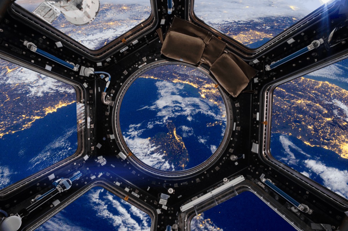 View of Earth at night from the cupola windows of the International Space Station, with city lights glowing beneath the clouds
